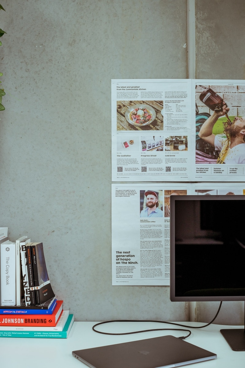 Pages of The Ninch newspaper pinned to a concrete wall above a desk in the ONETOO studio