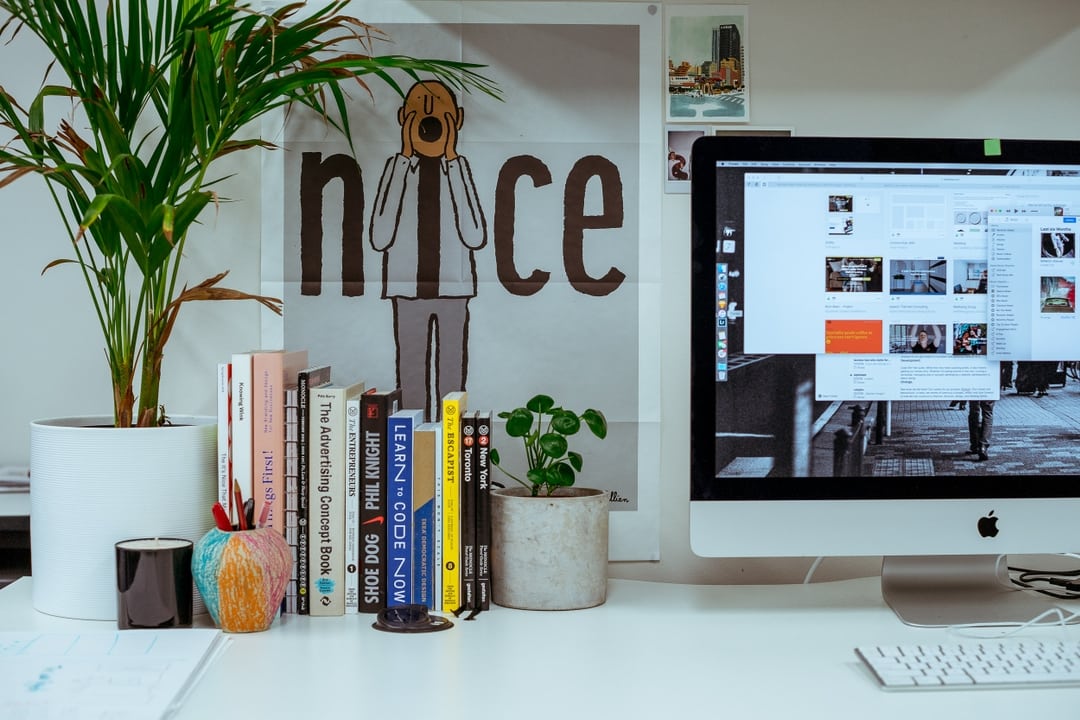 Desk in the ONETOO studio with an iMac, design books and a poster reading nice