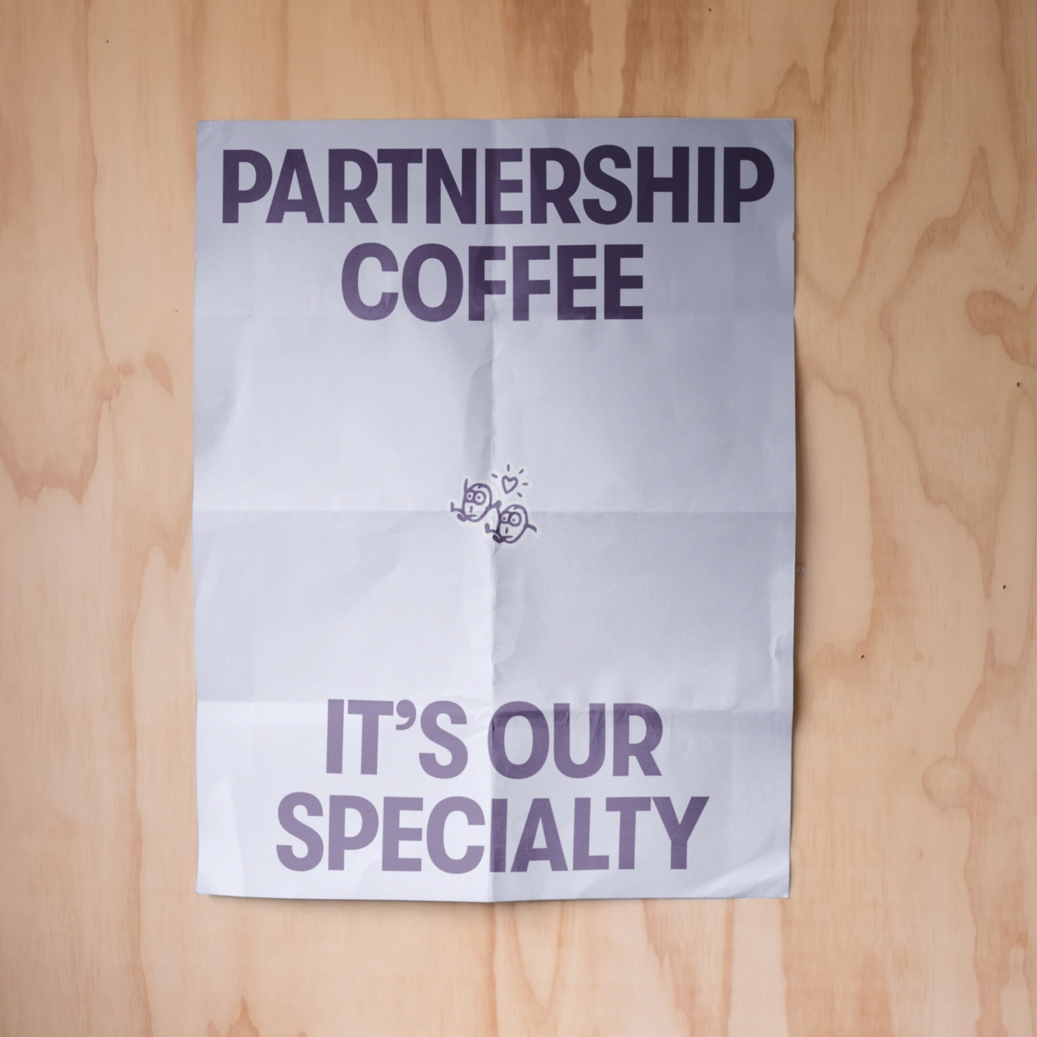 Poster Design for Commonfolk: Partnership Coffee, It's Our Specialty, on a folded poster against plywood